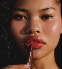 Bianca with glossy, tinted lips, holding up Espresso Lip Tint