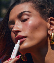 Hailey Bieber with glossy lips, applying peptide lip treatment in strawberry glaze