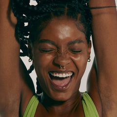model with glowing skin, smiling with eyes closed and hands in air