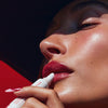 Hailey Bieber with glossy lips, applying peptide lip treatment in strawberry glaze