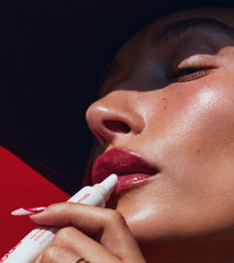 Hailey Bieber with glossy lips, applying peptide lip treatment in strawberry glaze
