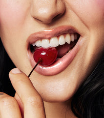 close up of model wearing peptide lip treatment with glossy lips, biting into a cherry