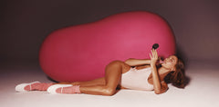 Hailey Bieber laying in front of a jumbo jelly bean, applying lip tint in jelly bean