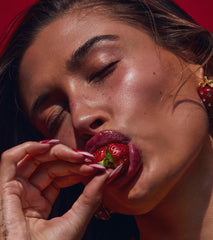 Hailey Bieber with glossy lips, biting into a strawberry