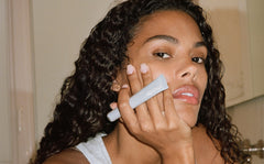 Tina Kunakey with glazed lips, holding peptide lip treatment