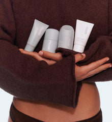 Person holding four mini rhode skincare products wearing with a brown sweater.